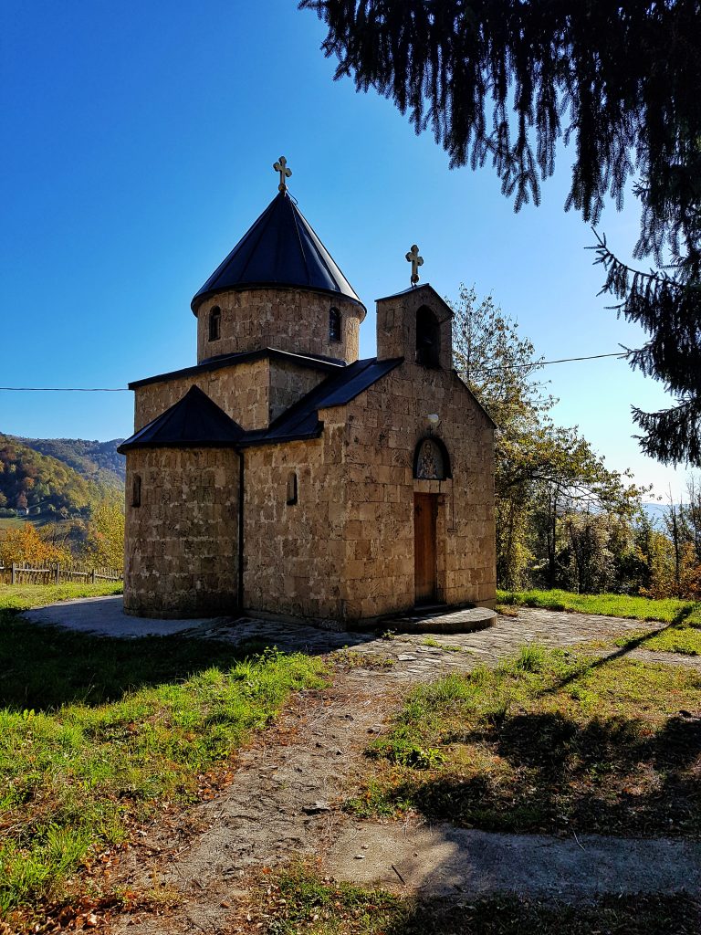 Mala kamena crkva u Sopotnici kod Prijepolja pod vedrim plavim nebom, okružena zelenilom i četinarima