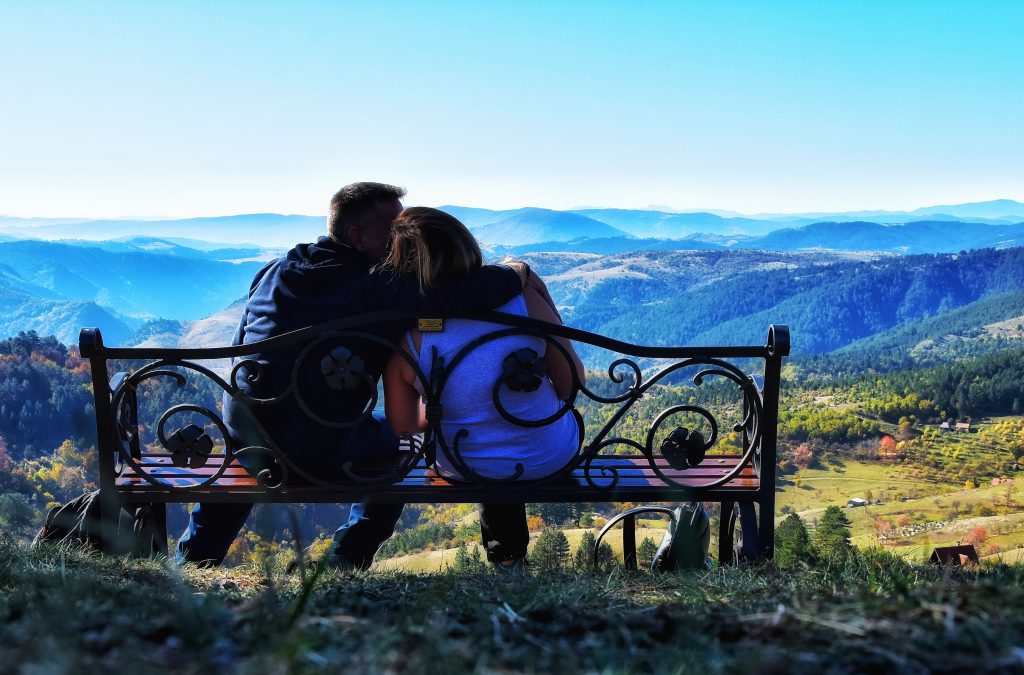 Par sedi na ukrašenoj drvenoj klupi na vidikovcu Dobroselica, posmatrajući panoramu Zlatibora pod vedrim nebom