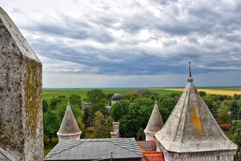 Panoramski pogled sa terase dvorca Fantast na ravnicu Vojvodine, krovove sa šiljatim kulama i kapelu u daljini.