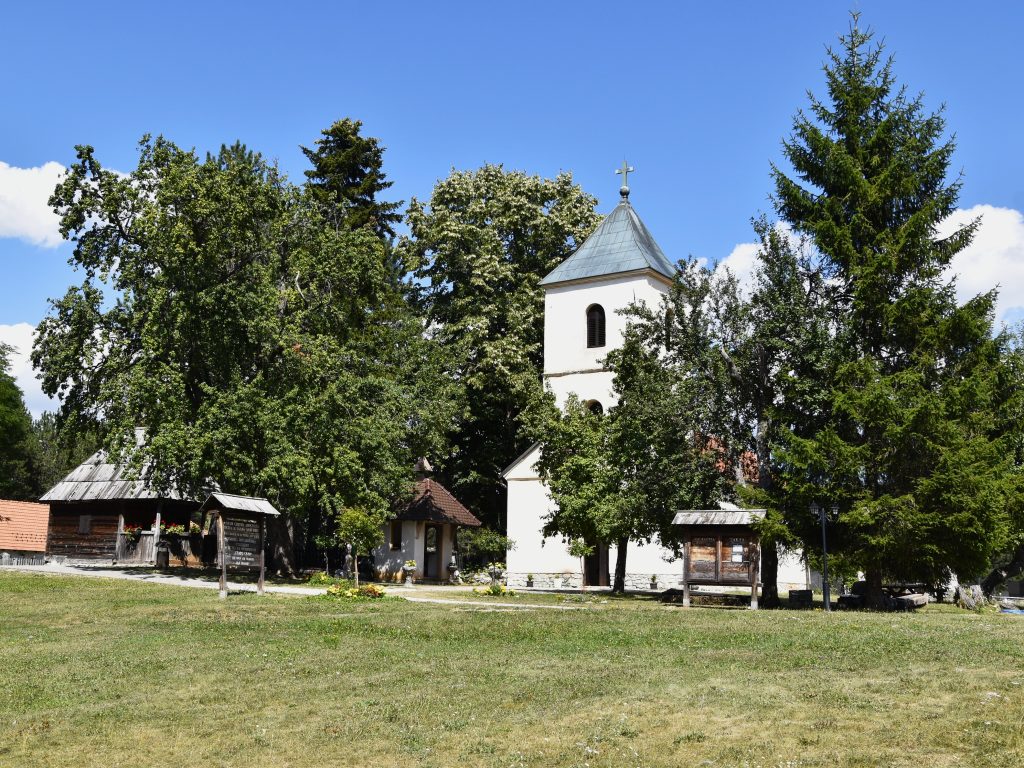 Pravoslavna crkva Svetih apostola Petra i Pavla u Sirogojnu uokvirena visokim cetinarima i zelenilom