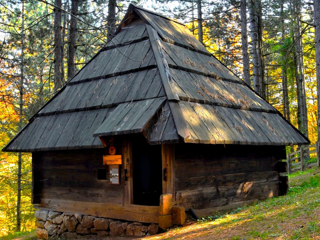 Drvena planinska koliba stan sa visokim krovom od dasaka u gustoj borovoj sumi etno sela Sirogojno