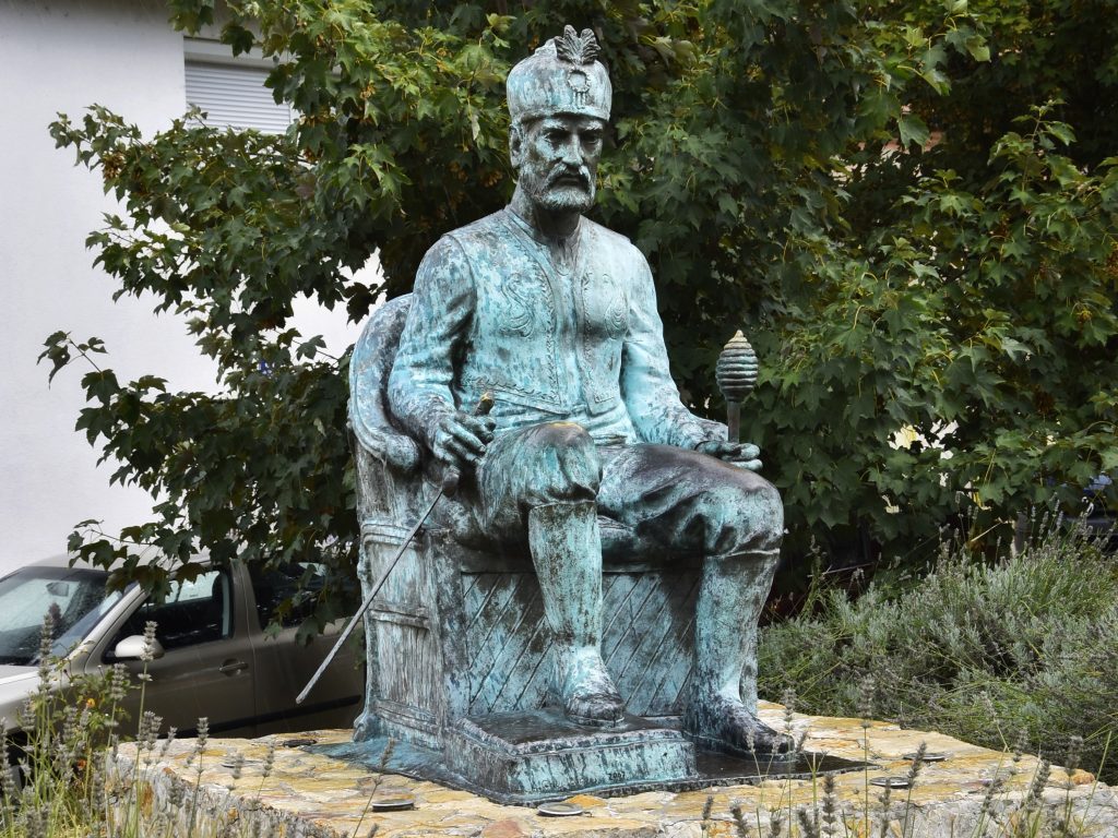 Bronzana statua Mehmed pase Sokolovica koji sedi na postolju u Visegradu pored mosta