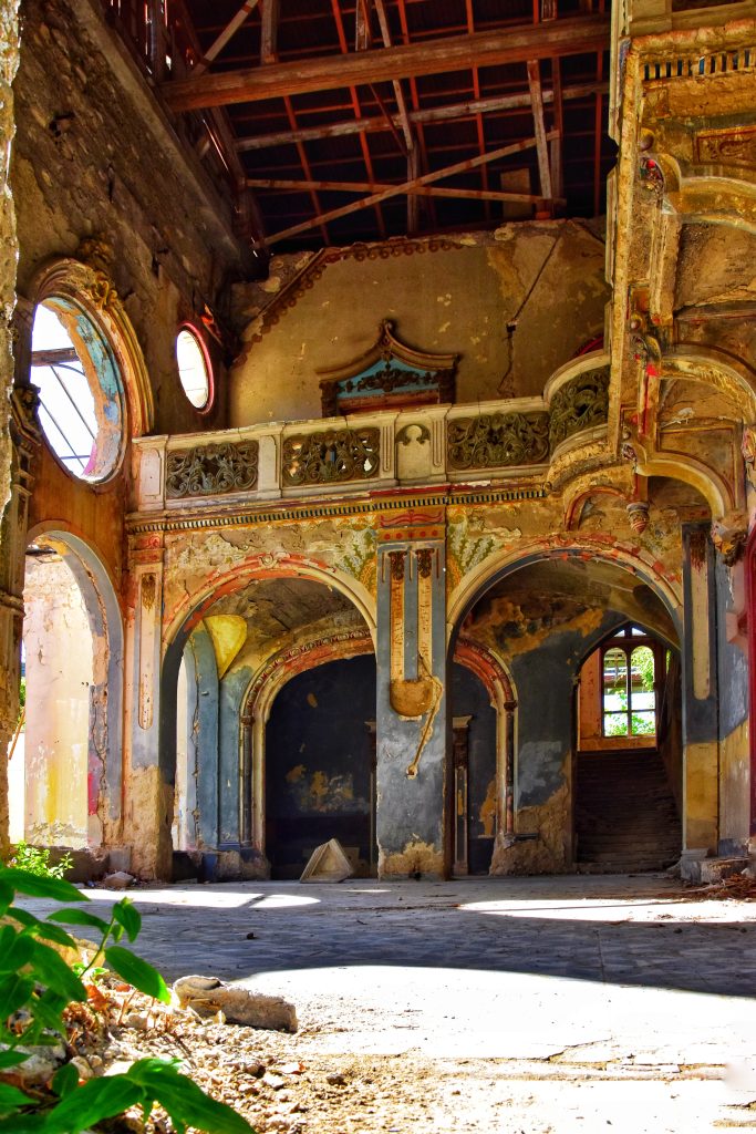 Unutrašnjost Špicerovog dvorca u Beočinu: pogled iz prizemlja na spratnu galeriju sa ukrasnim lukovima, tirkiznim zidovima i vidljivom krovnom konstrukcijom