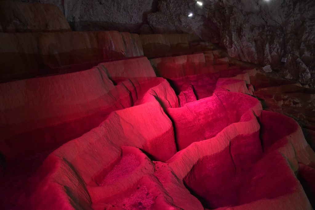 Serija kaskadnih bigrenih kada u dubini Stopica pecine pod dramaticnim roze i crvenim osvetljenjem