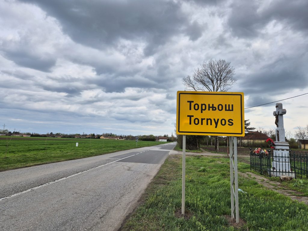 Tabla na ulazu u selo Tornjos na srpskom i madjarskom jeziku pod tmurnim nebom