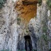 Monumentalni ulazni portal Potpecke pecine visine 50 metara u krecnjackoj litici, snimljen odozdo sa zelenilom u prvom planu