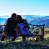 Par sedi na ukrašenoj drvenoj klupi na vidikovcu Dobroselica, posmatrajući panoramu Zlatibora pod vedrim nebom