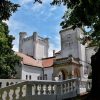 Pogled na beli dvorac Fantast sa neogotičkom kulom i ulaznim tremom, uokviren drvećem pod vedrim nebom.