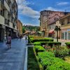 Pešačka zona u centru Valjeva, Ulica kneza Miloša sa cvetnim žardinjerama i prodavnicama pod vedrim nebom.