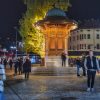 Osvetljeni Sebilj na Bascarsiji nocu sa prolaznicima i ukrasnim svetlima na drvecu u srcu starog grada