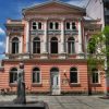 Zgrada stare stedionice u Valjevu sa ruzicastom fasadom i belim stubovima i spomenik Desanki Maksimovic u prvom planu