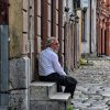 Stariji covek sa belom bradom sedi na kamenim stepenicama ispred stare kuce na kaldrmi u Tesnjaru, Valjevo